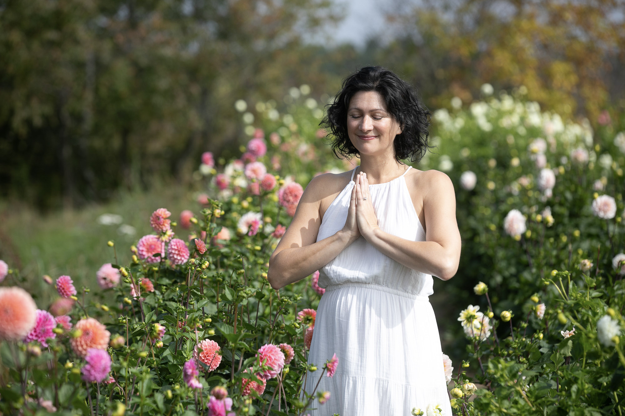 Christine Dion médite les yeux clos et les mains jointes dans un champ de dahlias colorés.