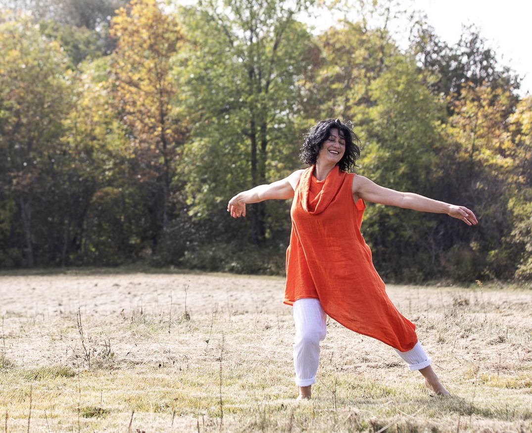 Christine Dion rayonnante danse dans un champ, les bras ouverts et le sourire éclatant.