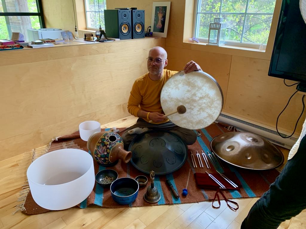 Un homme tient un tambour, entouré de handpans et bols chantants pour la méditation sonore.