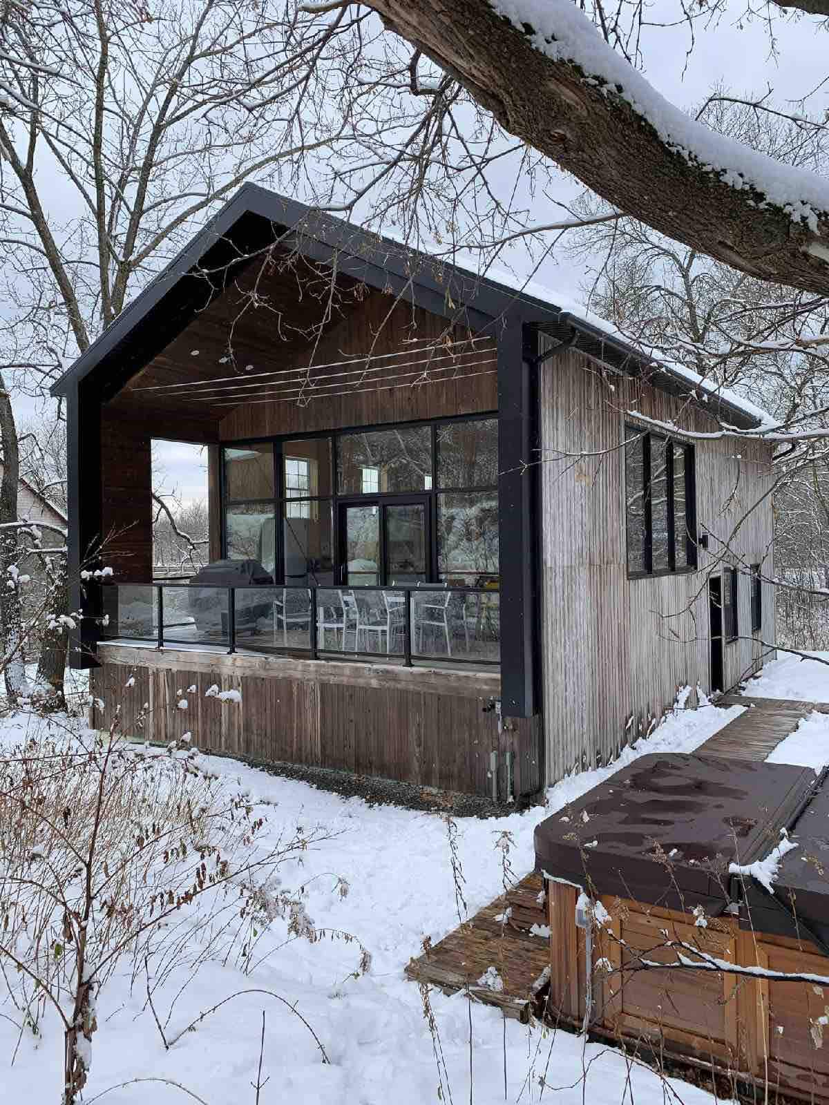 Chalet contemporain en bois et verre, avec une terrasse enneigée et un spa, au cœur d'un paysage hivernal.