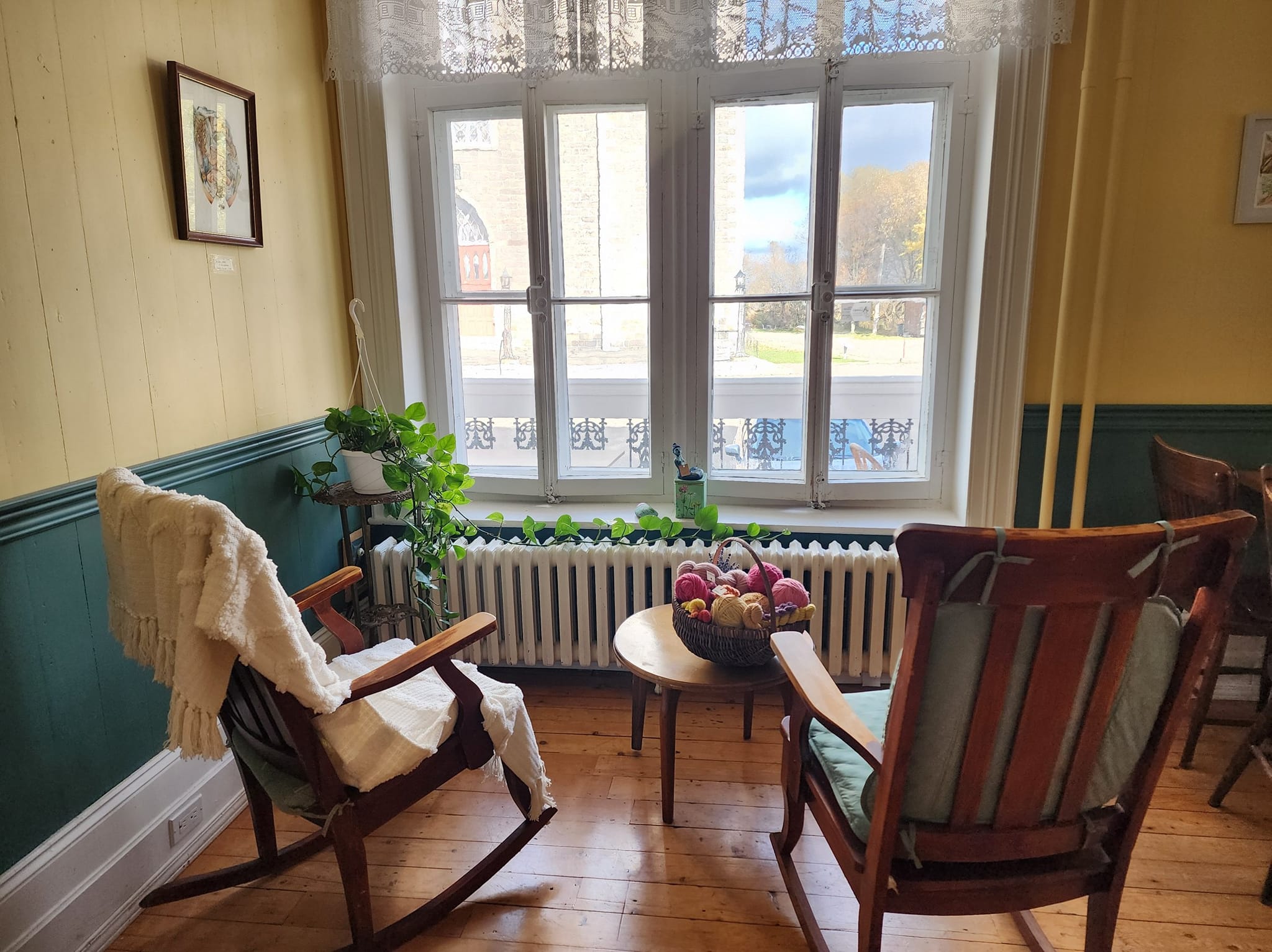 Intérieur confortable avec chaises en bois, plaid, panier de laine, plante verte et vue par la fenêtre.